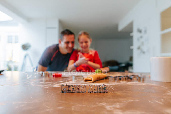 Father and daughter baking with Merry Christmas cookie cutters on table — Stock Photo