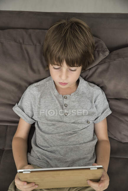 Niño sentado en el sofá con su tableta digital - foto de stock
