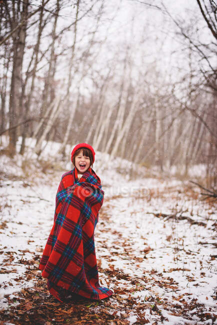 Portrait d'une fille enveloppée dans une couverture debout dans la neige riant — Photo de stock