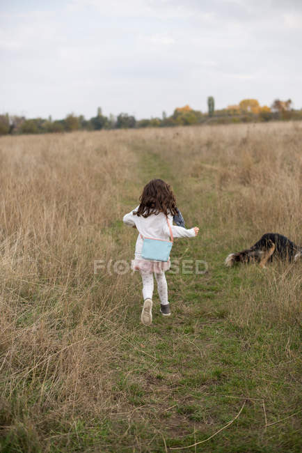 Girl running through field with her dog — Stock Photo