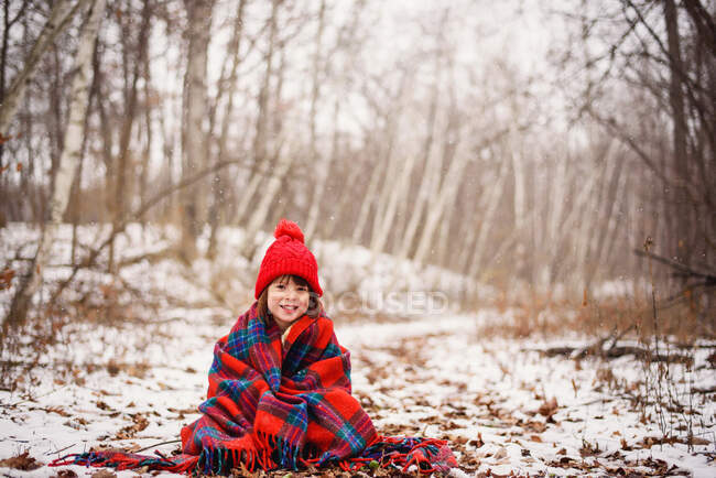 Fille assise dans la neige enveloppée dans une couverture — Photo de stock