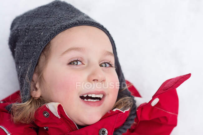 Adorable feliz chica acostada en la nieve - foto de stock