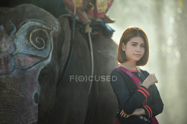 Retrato de una mujer de pie junto a un elefante, Tailandia - foto de stock