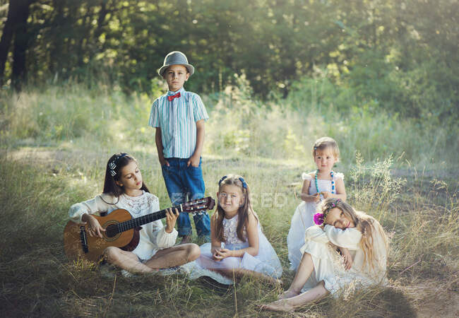 Gruppe von fünf Kindern im Wald, eines spielt Gitarre — Stockfoto