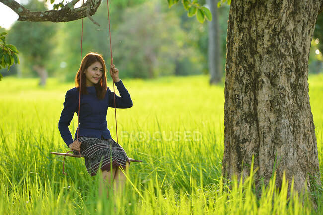 Donna seduta su un'altalena in un campo, Thailandia — Foto stock