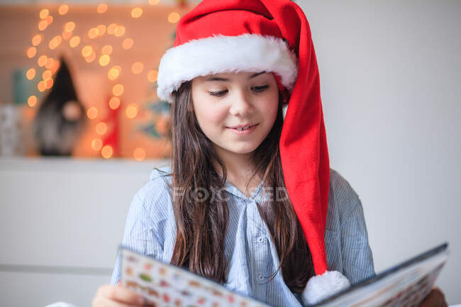 Portrait of a girl reading in a christmas santa hat — Stock Photo