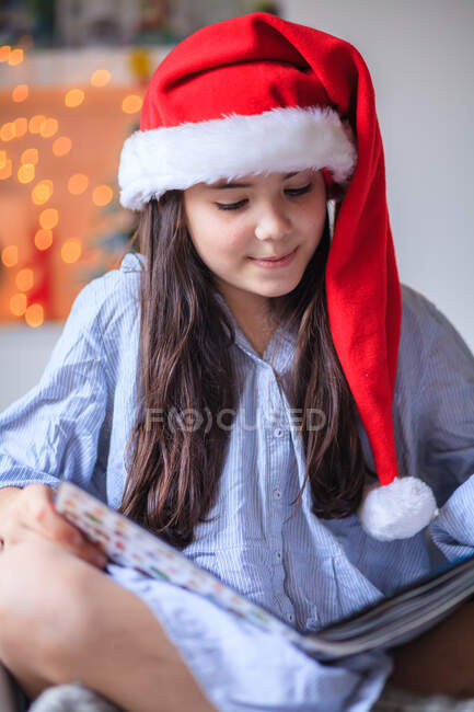 Retrato de uma menina lendo em um chapéu de Natal Papai Noel — Fotografia de Stock