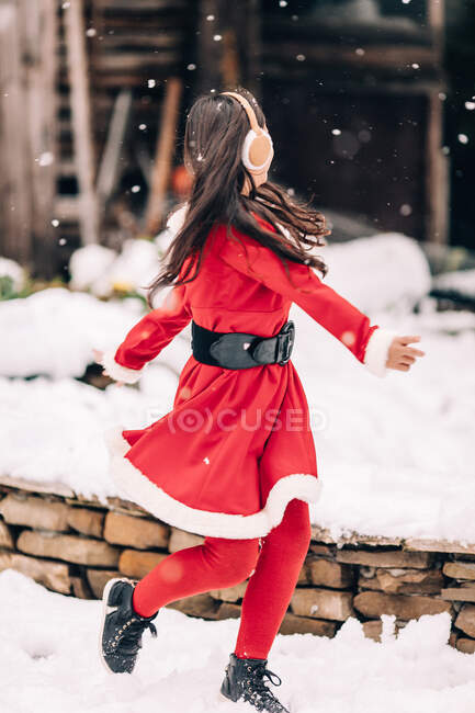 Улыбающаяся девушка в рождественском наряде Санты танцует на снегу — стоковое фото
