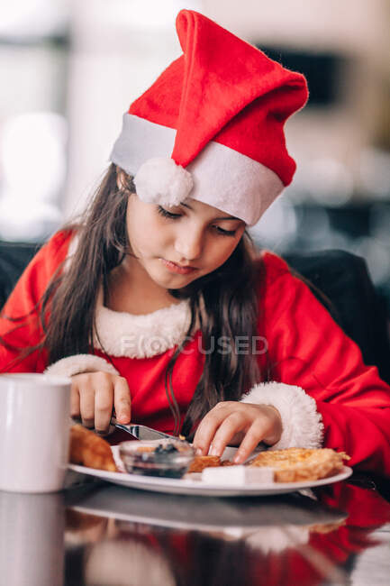 Ragazza in un vestito di Natale Babbo Natale e cappello mangiare la prima colazione — Foto stock