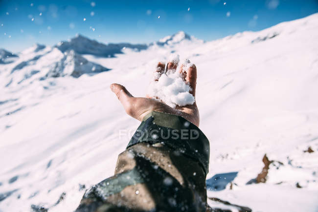 Mano de hombre sosteniendo nieve contra montañas cubiertas de nieve - foto de stock