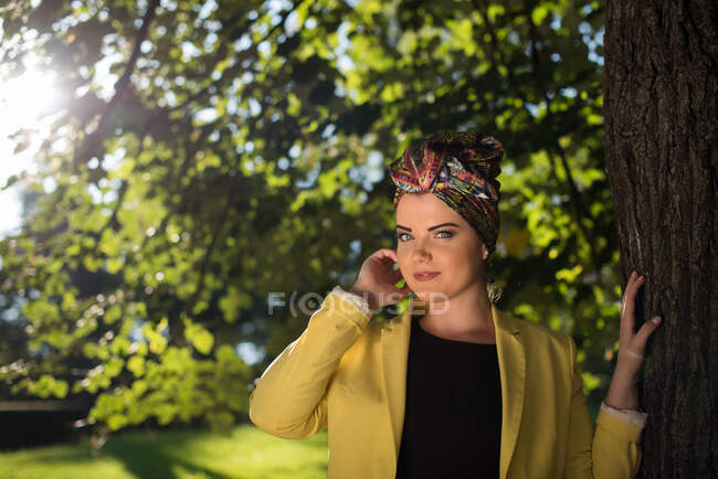 Mujer joven parada en el parque junto a un árbol - foto de stock