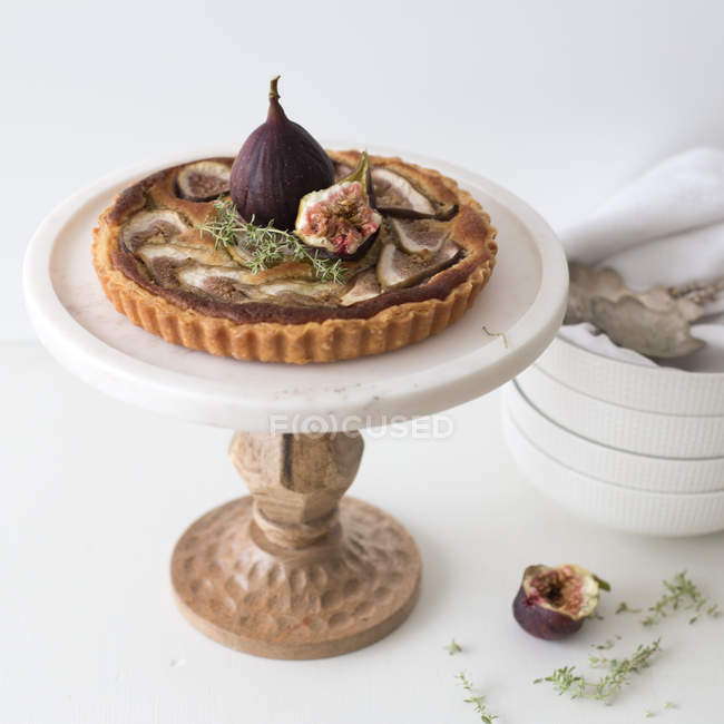 Fig tart on cake stand with stack of plates — Stock Photo