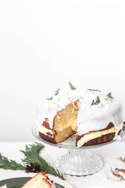 Close-up of a christmas coconut sponge cake with icing on a cakestand next to a slice of cake on a plate — Stock Photo