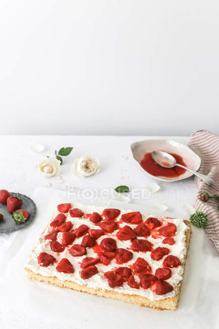 Sponge cake with strawberries and cream over table — Stock Photo