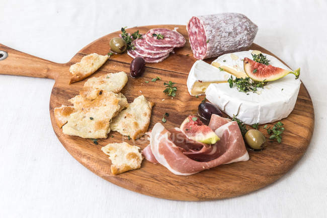 Cheese and cured meats on chopping board — Stock Photo