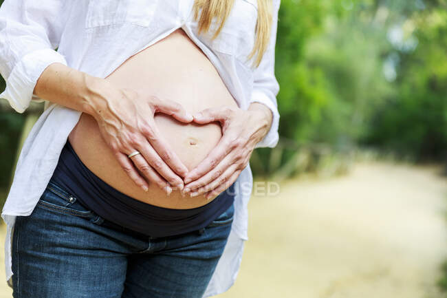 Frau macht Herzform mit ihren Händen auf ihrem Schwangerschaftsbauch — Stockfoto