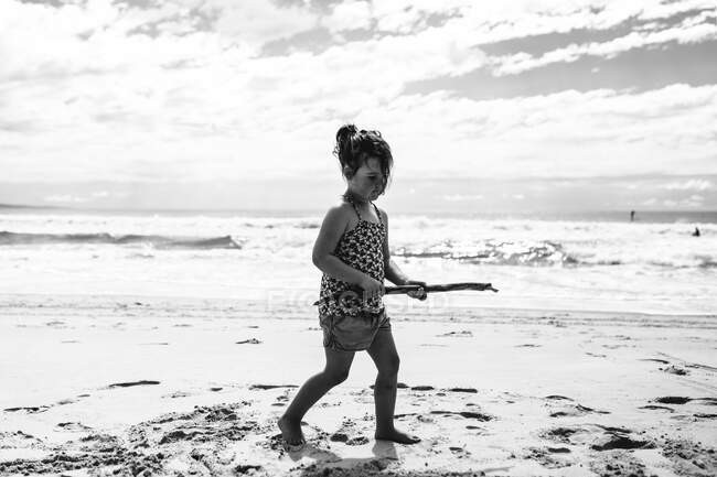 Дівчинка йде на пляжі, тримаючи палицю, Noosa Heads, Queensland, Australia — стокове фото