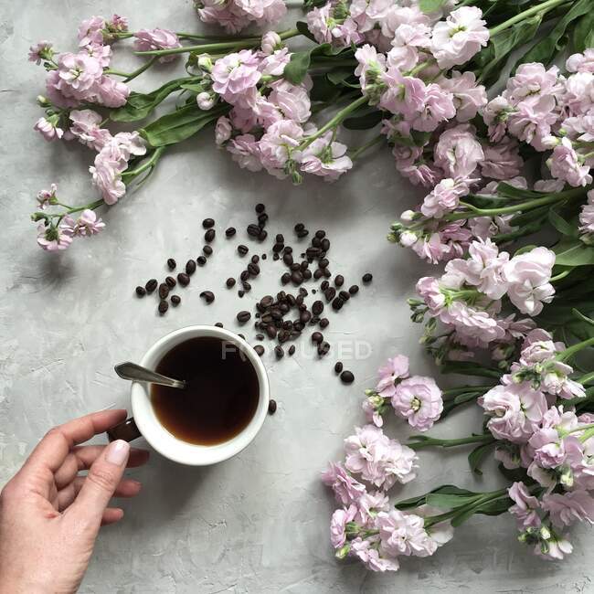 Mão de mulher com xícara de café e flores rosa — Fotografia de Stock