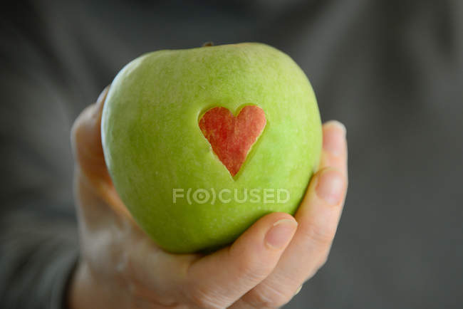 Женщина держит зеленое яблоко с красным сердцем — стоковое фото