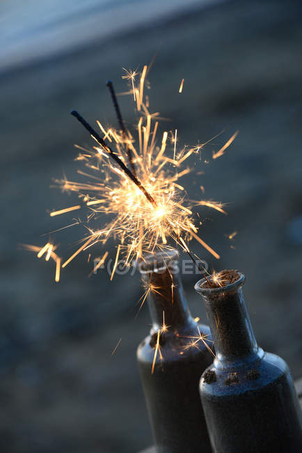 Closeup view of Lit sparklers in glass bottles on beach - foto de stock