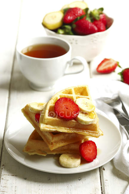 Chá e waffles belgas com morangos, banana e xarope de bordo — Fotografia de Stock