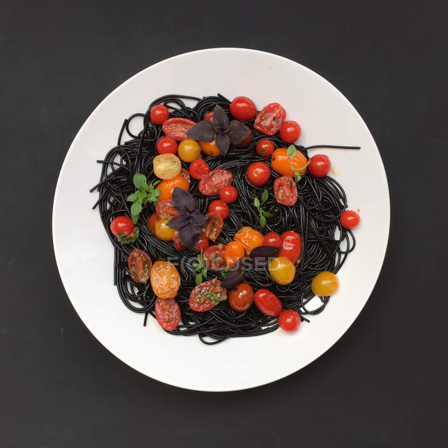 Чорна кальмарова макарони з свіжими помідорами і базилем. — стокове фото
