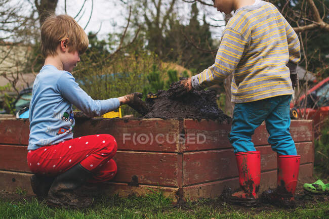 Dos chicos jugando con barro en el jardín - foto de stock