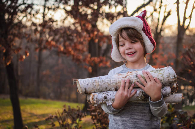 Menino feliz carregando lenha na natureza — Fotografia de Stock
