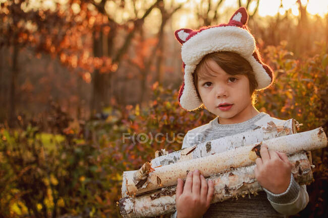 Menino carregando lenha na floresta outonal — Fotografia de Stock