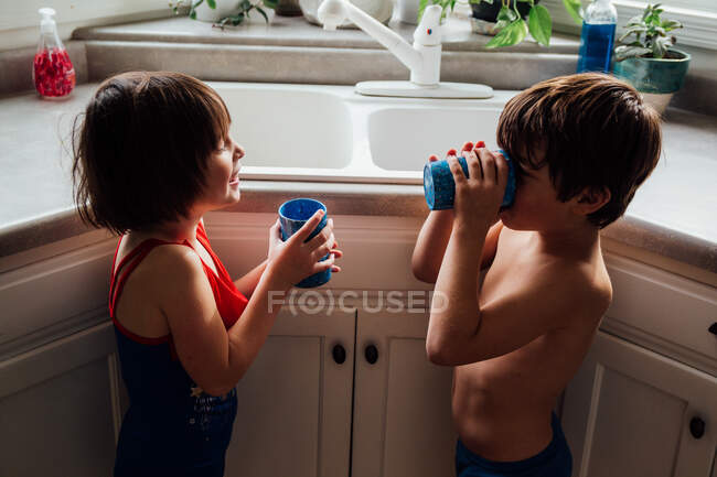 Boy and girl standing in kitchen drinking water — Stock Photo