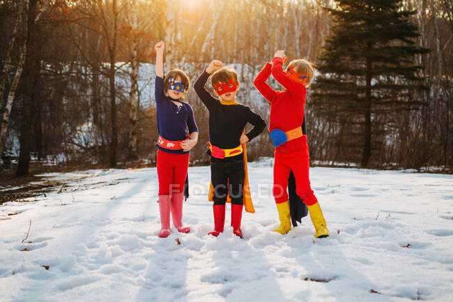 Троє дітей стоять на замерзлому озері в костюмах супергероїв — стокове фото