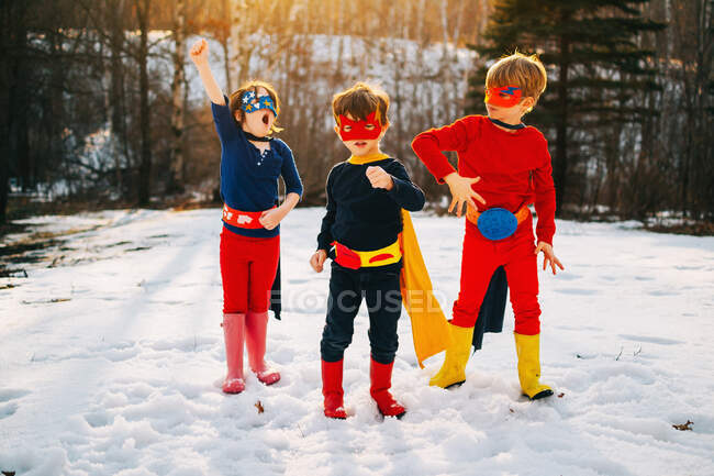 Tres niños de pie en el lago congelado vistiendo trajes de superhéroes - foto de stock
