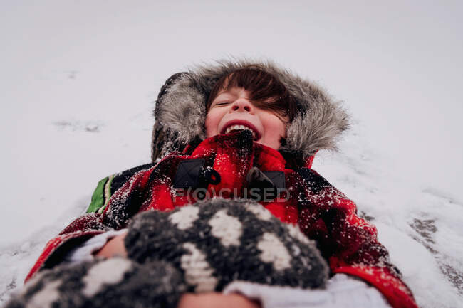 Menina feliz em parka com capuz deitado na neve — Fotografia de Stock