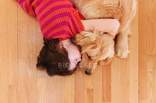 Девушка, лежащая на полу, обнимает золотистую собаку-ретривера — стоковое фото