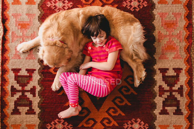 Vista aérea de la niña acostada en el suelo con un perro recuperador de oro - foto de stock