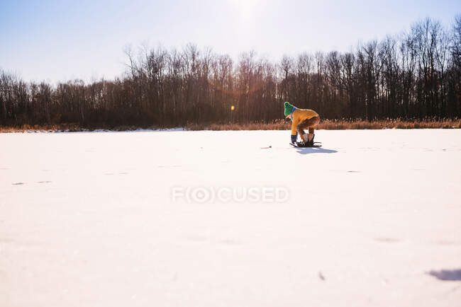 Junge in Schneeschuhen bückt sich — Stockfoto