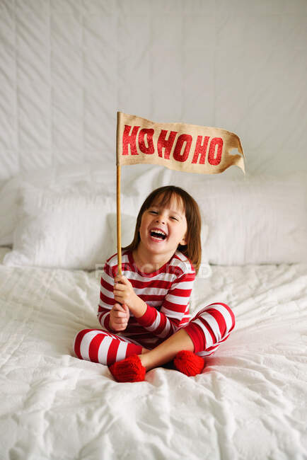 Menina sentada na cama segurando uma bandeira HoHoHo — Fotografia de Stock