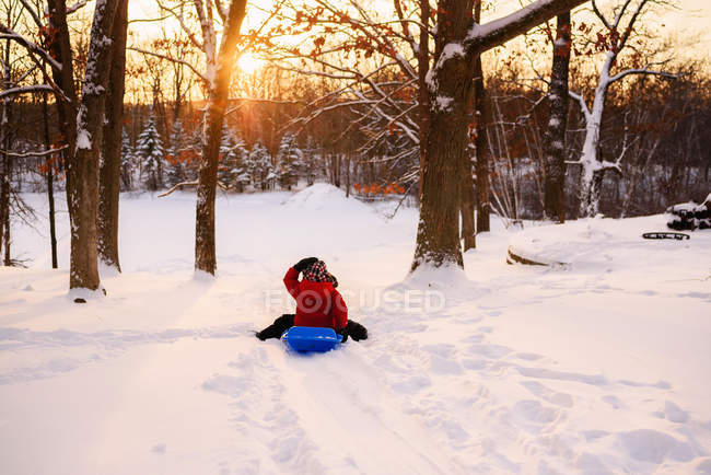 Boy sledding down hill at sunset — Stock Photo