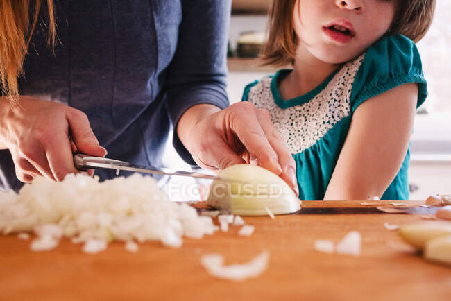 Mutter lehrt ihre Tochter Zwiebeln hacken — Stockfoto