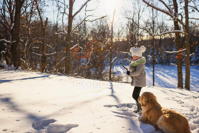 Девушка играет в снегу с золотистой собакой-ретривером — стоковое фото