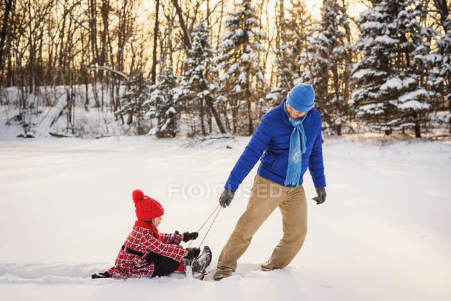 Padre tirando de la hija en un trineo en la nieve - foto de stock