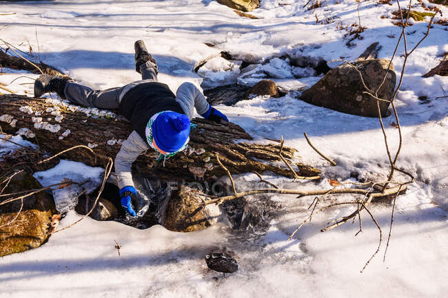 Boy lying on rocks by frozen creek — Stock Photo