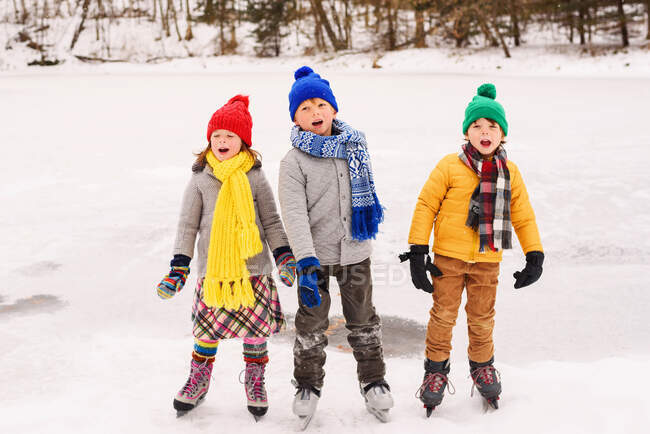 Three children on ice skates singing carols — Stock Photo