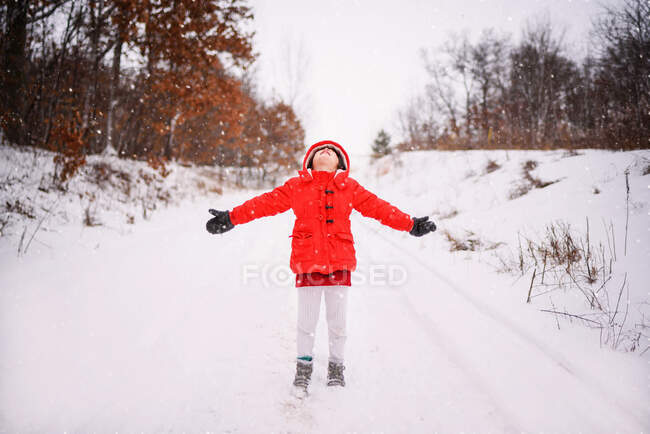 Девушка, стоящая с распростертыми руками и ловящая снег — стоковое фото