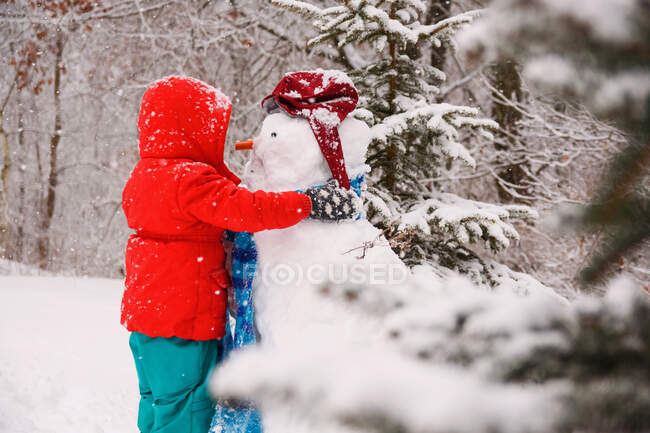 Chica abrazando a un muñeco de nieve - foto de stock