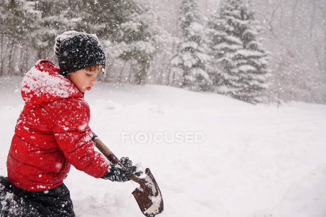 Мальчик убирает снег в зимнем лесу — стоковое фото
