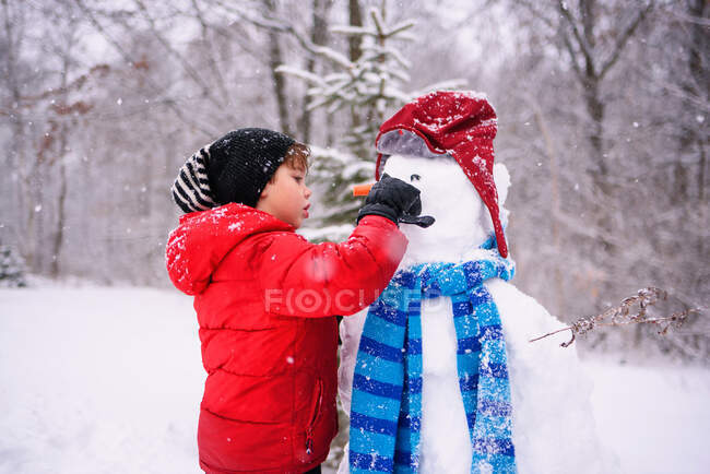 Menino construindo um boneco de neve na floresta de inverno — Fotografia de Stock