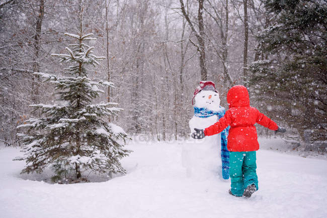 Девушка, стоящая рядом со снеговиком с распростертыми руками — стоковое фото