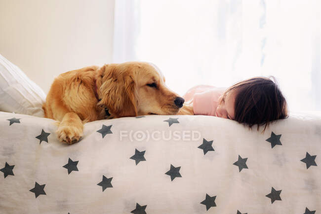 Fille couchée sur son lit avec un chien golden retriever — Photo de stock