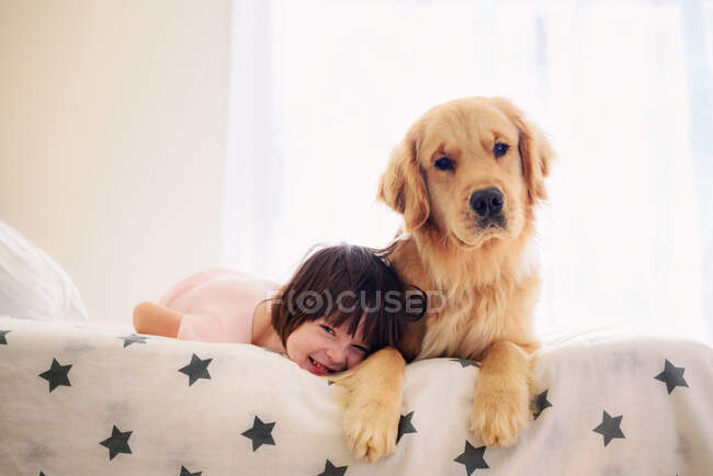 Девочка лежит на кровати с золотой собакой-ретривером — стоковое фото